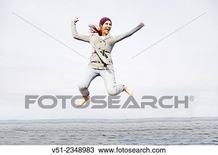 Young woman radiant with happiness jumping by the sea View Large Photo Image Stock Image - Young woman radiant with happiness jumping by the sea. Fotosearch