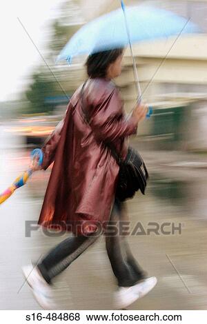 Stock Photo - "Young woman running across the street holding two umbrellas - Bucharest, Romania". Fotosearch