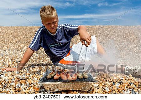 "A Boy Cooks Sausages On The Beach, Seaford, Sussex, UK. " View Large Photo Image Stock Image - "A Boy Cooks Sausages On The Beach, Seaford, Sussex, UK. ". Fotosearch