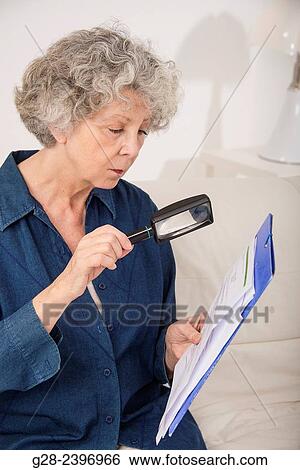 Beautiful senior woman holding a magnifying glass in one hand to read papers which she holds in the other hand View Large Photo Image Stock Photograph - Beautiful senior woman holding a magnifying glass in one hand to read papers which she holds in the other hand. Fotosearch