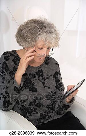"Beautiful senior woman reading an electronic book, on a Kindle, at home, wearing glasses" View Large Photo Image Stock Photo - "Beautiful senior woman reading an electronic book, on a Kindle, at home, wearing glasses". Fotosearch