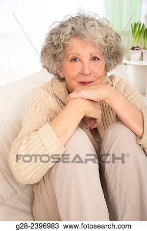 "Beautiful senior woman sitting on her sofa, smiling, with plants in the background at home" View Large Photo Image Stock Image - "Beautiful senior woman sitting on her sofa, smiling, with plants in the background at home". Fotosearch