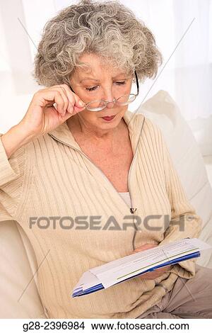 Beautiful senior woman with glasses reading papers sitting on her sofa at home View Large Photo Image Picture - Beautiful senior woman with glasses reading papers sitting on her sofa at home. Fotosearch