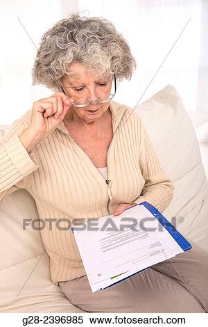 Beautiful senior woman with glasses reading papers sitting on her sofa at home View Large Photo Image Stock Photography - Beautiful senior woman with glasses reading papers sitting on her sofa at home. Fotosearch