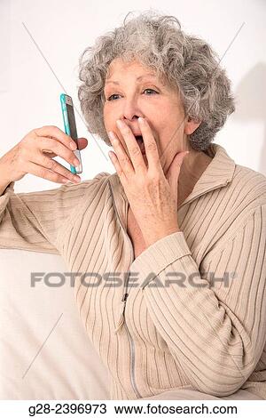 Stock Image - Beautiful surprised senior woman on the phone with hand in front of her mouth. Fotosearch