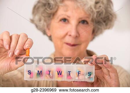 Stock Photo - "Beautiful surprised senior woman holding a tablet in one hand, and a daily tablet distributor in the other hand and smiling". Fotosearch