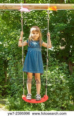 Stock Photograph - Happy 6 year old girl standing on a seat of a garden swing.. Fotosearch