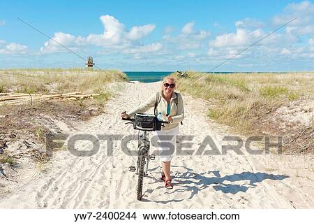 Picture - "Happy woman walking with her bicycle from Baltic sea beach, Poland". Fotosearch