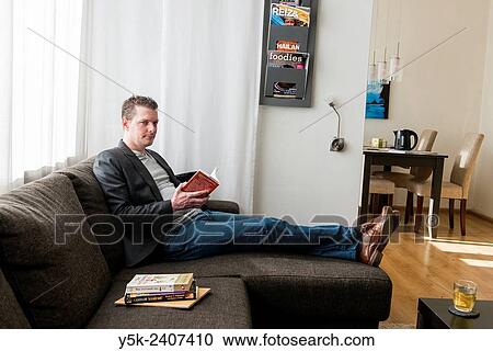 "Tilburg, Netherlands. Young man sitting in his living room, reading a book, while being a regular hosts for international travellers within the global Couch Surfing community. " View Large Photo Image Stock Image - "Tilburg, Netherlands. Young man sitting in his living room, reading a book, while being a regular hosts for international travellers within the global Couch Surfing community. ". Fotosearch