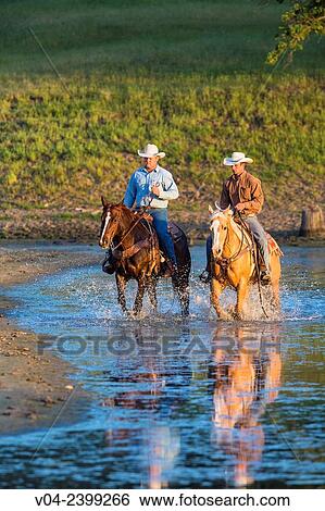 Stock Photograph - "Two wranglers Cowboys on horses, riding through water, California, USA". Fotosearch