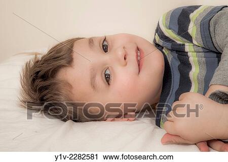 Young boy lying on a bed. View Large Photo Image Stock Image - Young boy lying on a bed.. Fotosearch