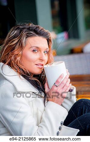 A 27 year old brunette woman sitting at an outdoor cafe and holding a white mug of hot chocolate looking at the camera. View Large Photo Image Stock Photography - A 27 year old brunette woman sitting at an outdoor cafe and holding a white mug of hot chocolate looking at the camera.. Fotosearch