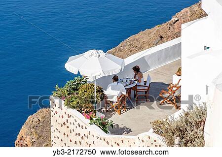 Stock Image - A Couple Eating Breakfast On A Terrace, Oia, Santorini, Greek Islands, Greece.. Fotosearch