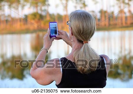 A senior woman taking scenic pictures beside a lake with a camera phone, ipod or iphone View Large Photo Image Stock Photography - A senior woman taking scenic pictures beside a lake with a camera phone, ipod or iphone. Fotosearch