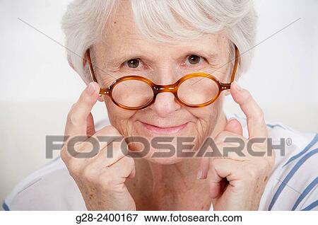 Stock Photo - Beautiful senior woman putting her glasses on her nose. Fotosearch