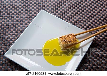 Stock Image - Chinese chopsticks dipping bread in olive oil. Close view.. Fotosearch