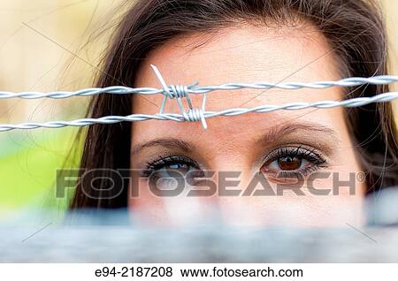 Eyes of a brunette woman looking through the barbed wire of a fence. View Large Photo Image Stock Photo - Eyes of a brunette woman looking through the barbed wire of a fence.. Fotosearch