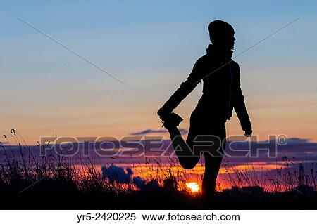 Stock Photography - Female jogger stretching at sunrise. Cowpen Woodland Park, Billingham, England, United Kingdom.. Fotosearch