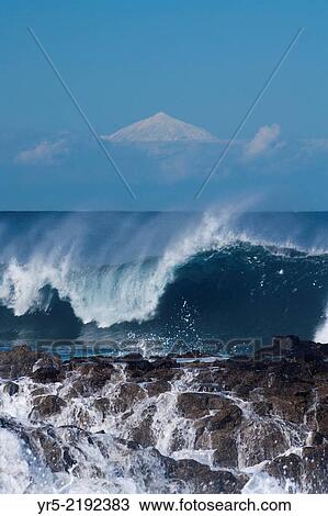 Stock Image - Huge wave crashing onto rocks at surfing spot, El Confital, Las Palmas, Gran Canaria, with snow covered El Teide on Tenerife in background. Gran Canaria, Canary Islands, Spain.. Fotosearch