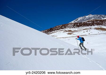 Stock Photograph - Man walking in snow covered Teide National Park on Tenerife, Canary Islands, Spain. Peak of El Teide visible in distance.. Fotosearch