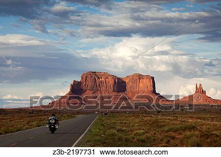 Stock Image - Motorcycle driving towards buttes in Monument Valley, Utah, USA.. Fotosearch