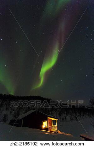 Stock Image - Northern light, Aurora borealis with a cottage, cabin with lights from window and snow landscape in Kiruna, Swedish lapland.. Fotosearch