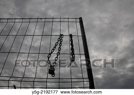Stock Photo - padlock with chain on open gate fence with dark sky. Fotosearch