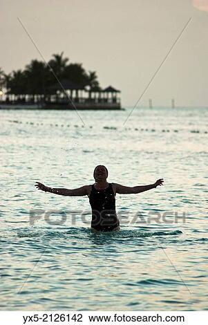 Stock Image - Silhouette of a woman bathing on a beach at sunset.. Fotosearch