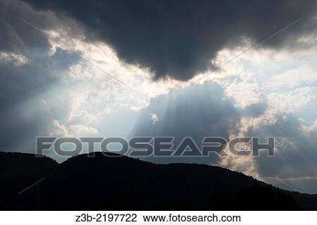 Stock Image - Sun rays stream from a cloud above the Adirondack Mountains near Ticonderoga in upstate NY, USA, North America. Fotosearch