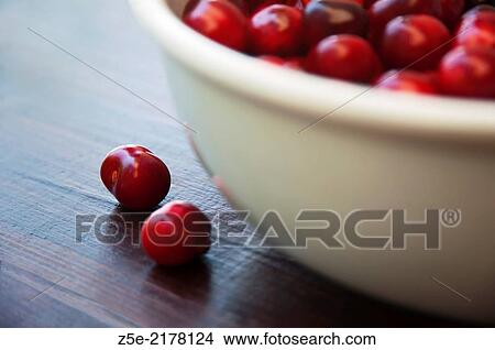 Picture - Two cherries next to a bowl full of cherries.. Fotosearch