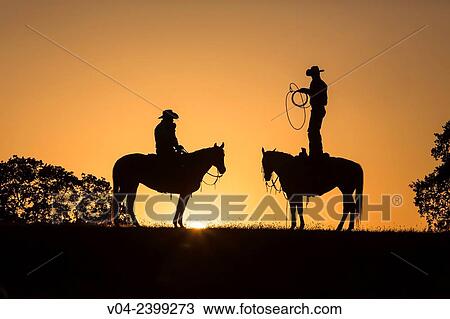 Stock Image - Two wranglers (cowboys) on horses at sunset, California, USA. Fotosearch