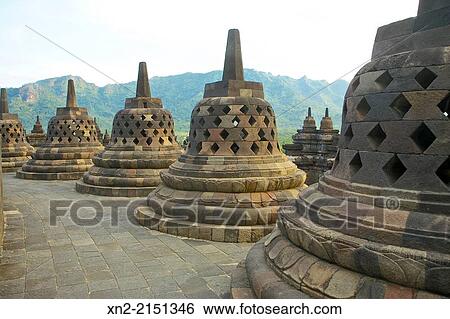 View of the Menoreh Hills and Kedu Plain through some of the 72 stupas atop the 9th-Century Mahyana Buddhist Temple at Borobudur, Central Java, Indonesia View Large Photo Image Stock Photograph - View of the Menoreh Hills and Kedu Plain through some of the 72 stupas atop the 9th-Century Mahyana Buddhist Temple at Borobudur, Central Java, Indonesia. Fotosearch