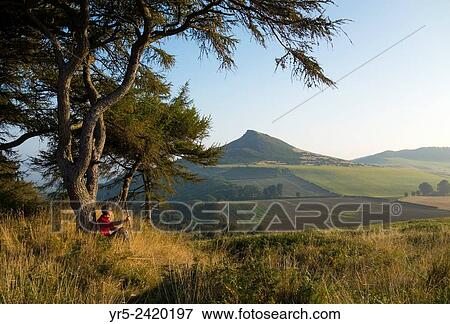 Stock Photo - Walker on Cliff Ridge at sunrise with Roseberry Topping in distance. North York Moors, National Park, England, United Kingdom.. Fotosearch
