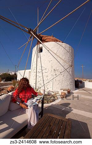 Stock Photo - Woman sitting at the open-air cafe in front of a windmill, Koufonissi, Cyclades Islands, Greek Islands, Greece, Europe.. Fotosearch