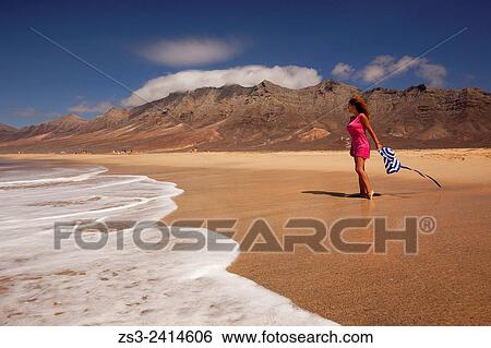 Stock Photograph - Woman walking on the beach of Cofete, Fuerteventura, Spain, Europe.. Fotosearch