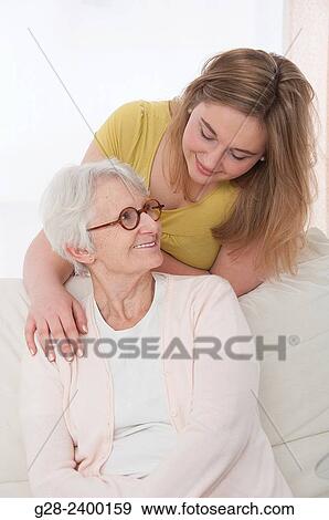 Stock Photo - Young medical help or granddaughter holding beautiful senior woman by her shoulders, and smiling to her, at home. Fotosearch