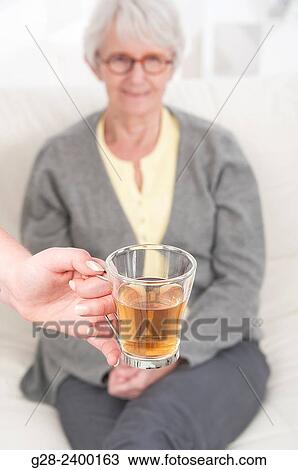 Young nurse or help or grand daughter holding a glass of tea, for patient or grandmother who is laughing in the background View Large Photo Image Stock Image - Young nurse or help or grand daughter holding a glass of tea, for patient or grandmother who is laughing in the background. Fotosearch