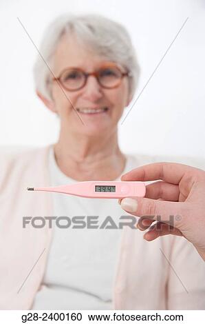 Stock Image - Young nurse or help or granddaughter holding a medical thermometer for patient or grandmother who is laughing in the background. Fotosearch