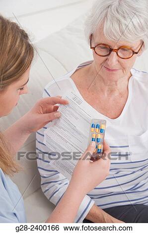 Young nurse or help or granddaughter reading prescription paper, and holding tablets, for patient or grandmother who is laughing in the background View Large Photo Image Stock Photograph - Young nurse or help or granddaughter reading prescription paper, and holding tablets, for patient or grandmother who is laughing in the background. Fotosearch