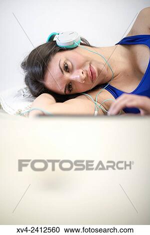 Young Woman relaxing on her sofa and listening to music on her tablet with Headphones. View Large Photo Image Stock Image - Young Woman relaxing on her sofa and listening to music on her tablet with Headphones.. Fotosearch