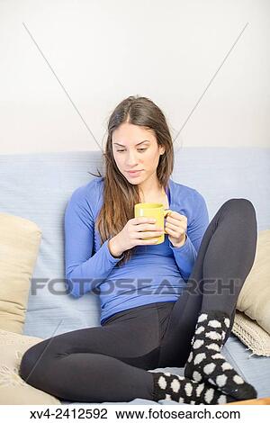 Young Woman relaxing on her sofa and drinking hot beverage. View Large Photo Image Stock Image - Young Woman relaxing on her sofa and drinking hot beverage.. Fotosearch