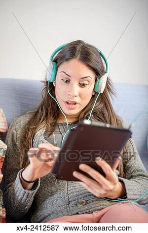 Young Woman relaxing on her sofa and listening to music on her tablet with Headphones. View Large Photo Image Stock Photo - Young Woman relaxing on her sofa and listening to music on her tablet with Headphones.. Fotosearch