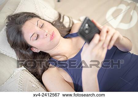 Young Woman relaxing on her sofa chating with her smartphone. View Large Photo Image Stock Photo - Young Woman relaxing on her sofa chating with her smartphone.. Fotosearch