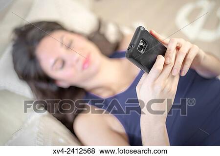 Young Woman relaxing on her sofa chating with her smartphone. View Large Photo Image Stock Photo - Young Woman relaxing on her sofa chating with her smartphone.. Fotosearch