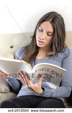 Picture - Young Woman studing English on her sofa.. Fotosearch