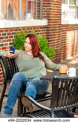 A 24 year old brunette woman sitting at an outdoor cafe looking at her cell phone. View Large Photo Image Picture - A 24 year old brunette woman sitting at an outdoor cafe looking at her cell phone.. Fotosearch