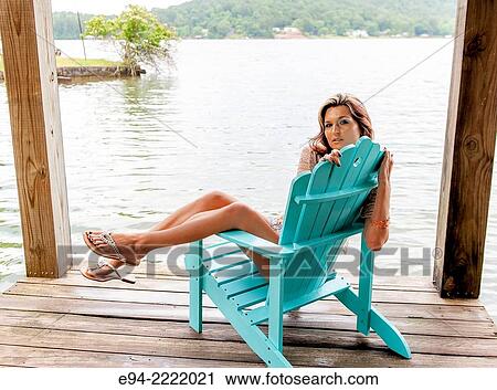 A 27 year old brunette woman sitting on an Adirondack chair on a dock by a lake. View Large Photo Image Stock Image - A 27 year old brunette woman sitting on an Adirondack chair on a dock by a lake.. Fotosearch