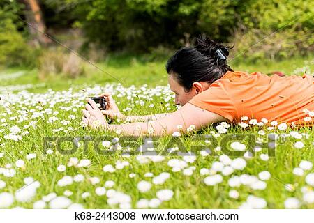 Stock Photo - A woman, 50, taking photos as she lies on the grass in a park on Saturna Island, Gulf Islands, British Columbia, Canada.. Fotosearch