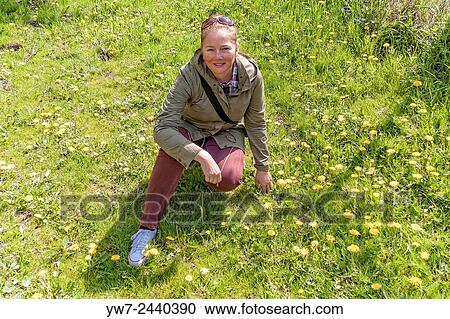 Stock Image - Adult woman sqauatting among dandelion flowers in Mlociny park, Warsaw, Poland.. Fotosearch