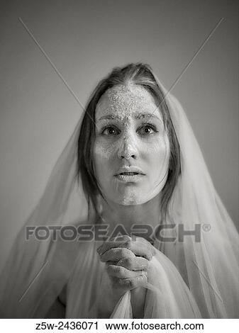 Stock Image - Close up woman face and ashes, she wearing white canvas and she praying, tinted black and white image, intentional noise added.. Fotosearch